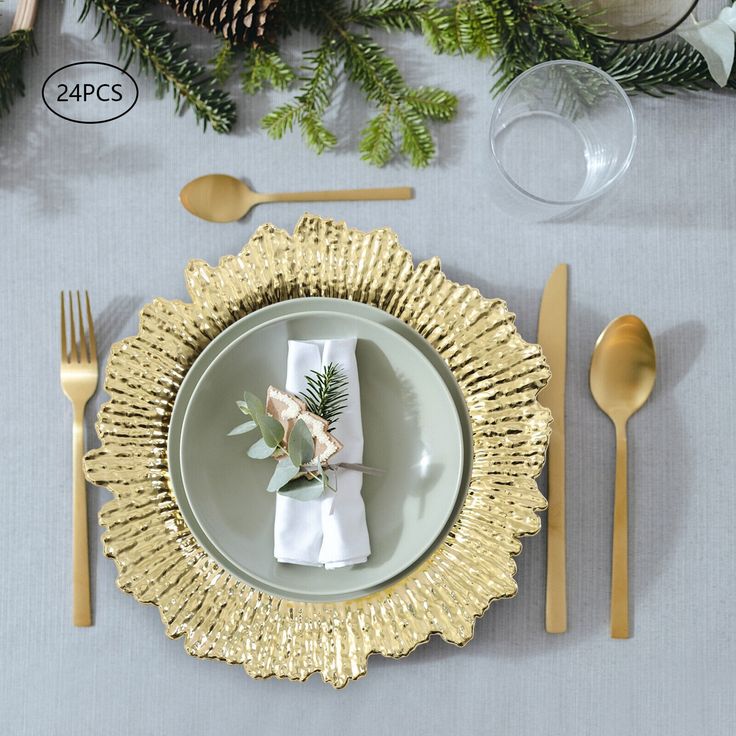 a place setting with gold plates and silverware, pine cones, greenery and napkins