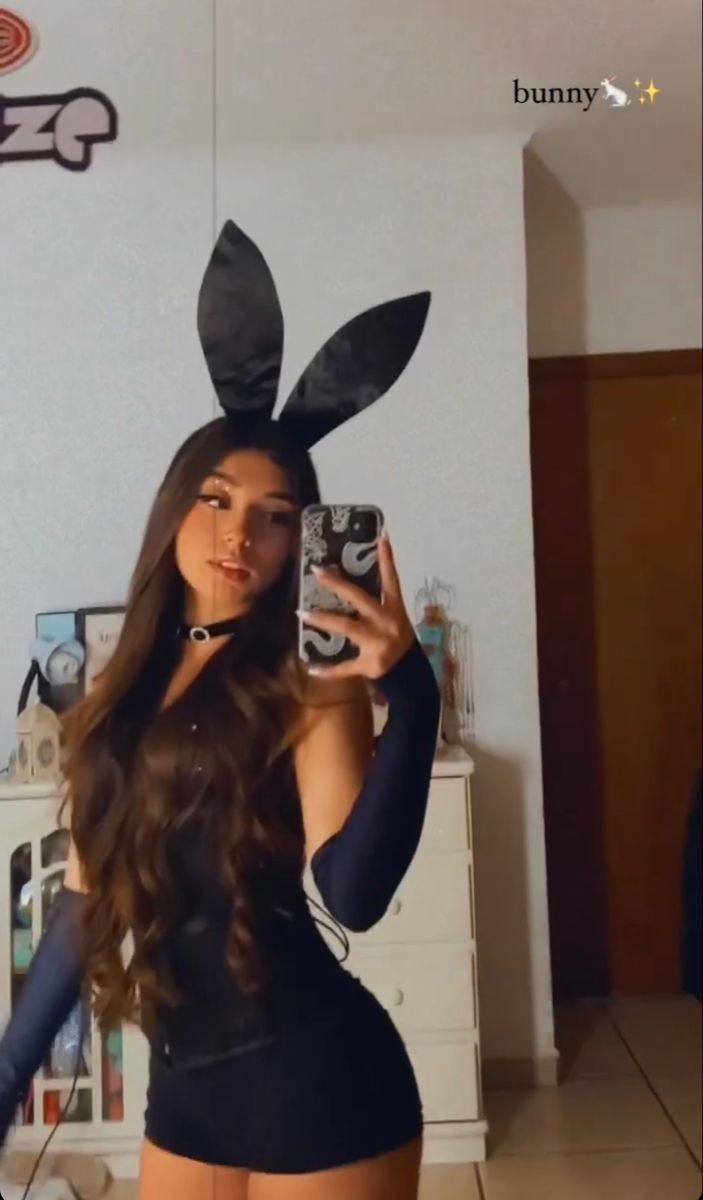 a woman in bunny ears taking a selfie with her cell phone and holding a camera