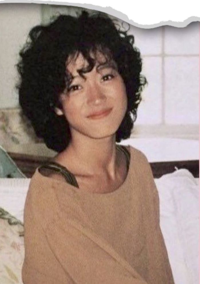 an old photo of a woman with short hair and brown shirt on, smiling at the camera