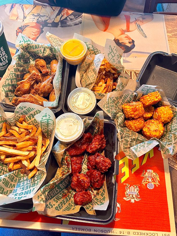 several trays of food including chicken wings, french fries and ketchup on a table