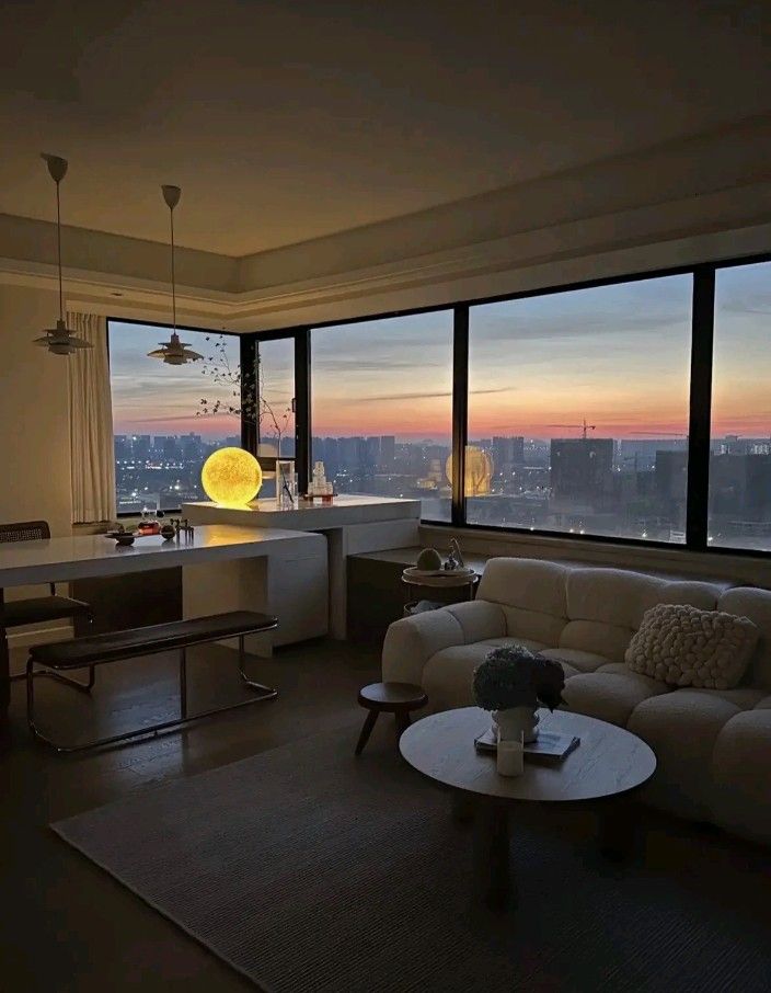 a living room filled with furniture and large windows overlooking the city at sunset or dawn