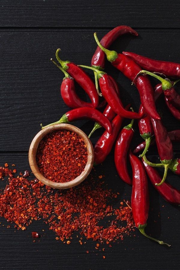 some red peppers are next to a small wooden bowl with chili seasoning on it