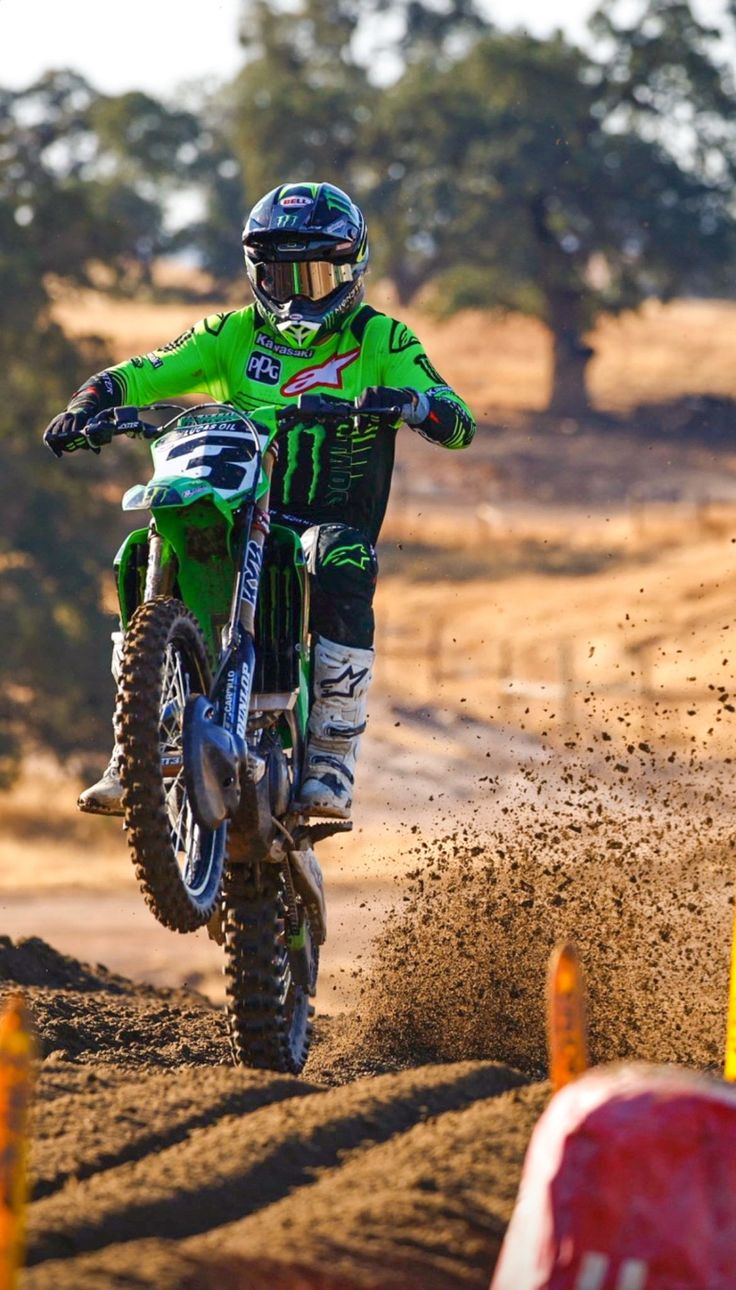 a man riding on the back of a dirt bike down a dirt road next to orange cones