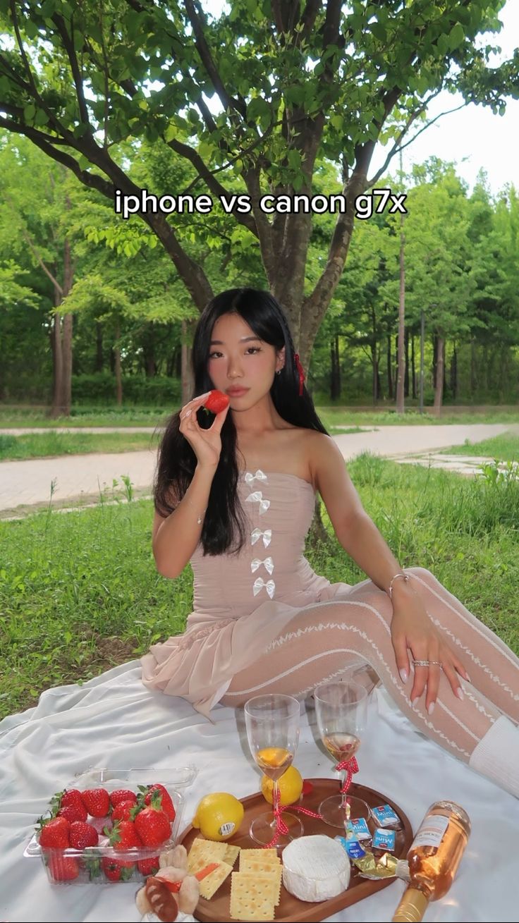 a woman sitting on the ground with food and drinks in front of her, next to a tree