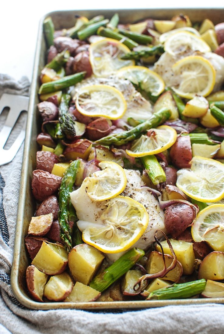 a pan filled with potatoes, asparagus and lemons