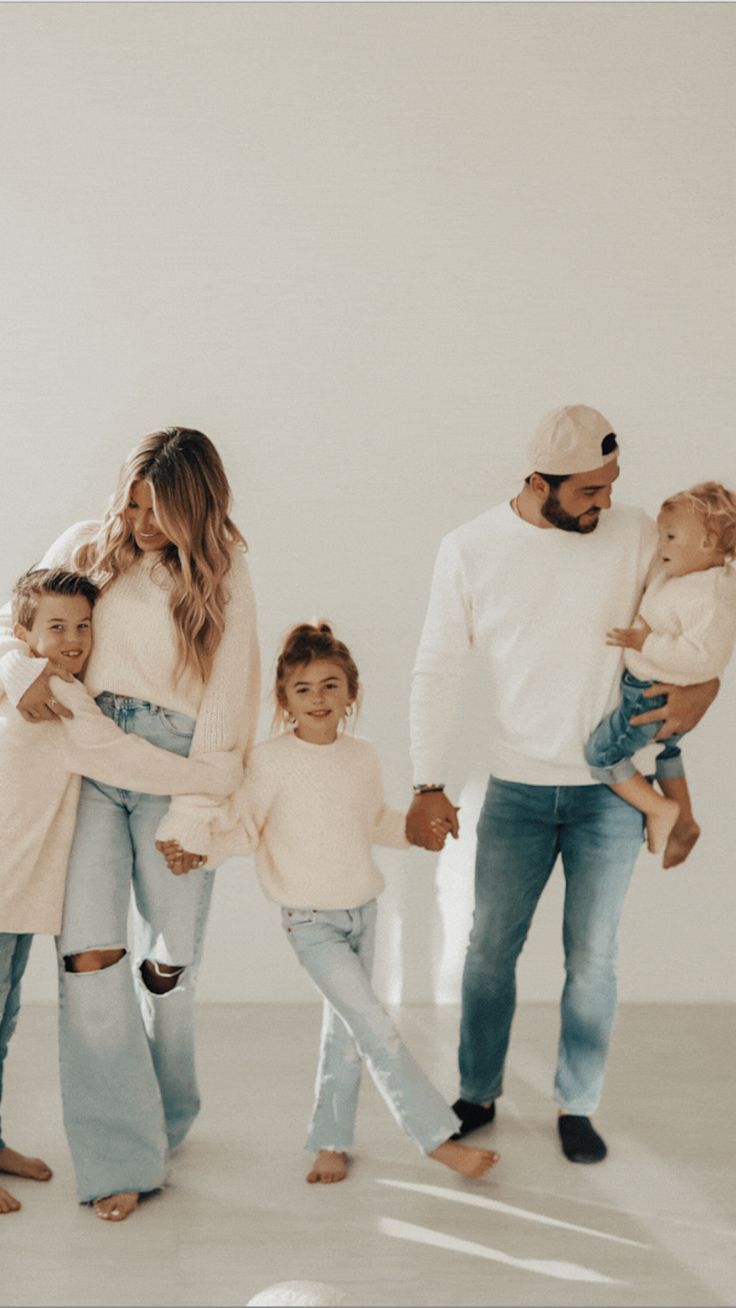 a man and woman holding two children while standing next to each other in front of a white wall