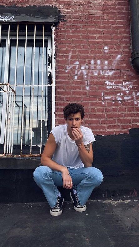 a young man sitting on the ground in front of a brick building with graffiti written on it