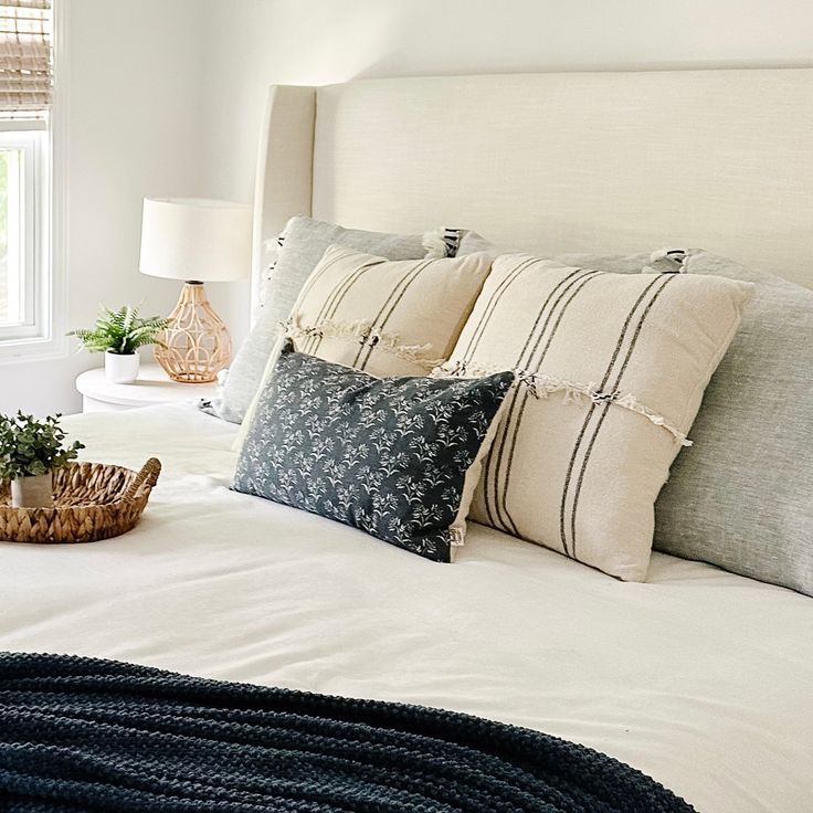 a bed with white linens and pillows in a bedroom next to a basket filled with plants