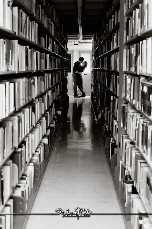 black and white photograph of two people kissing in a library with lots of books on the shelves