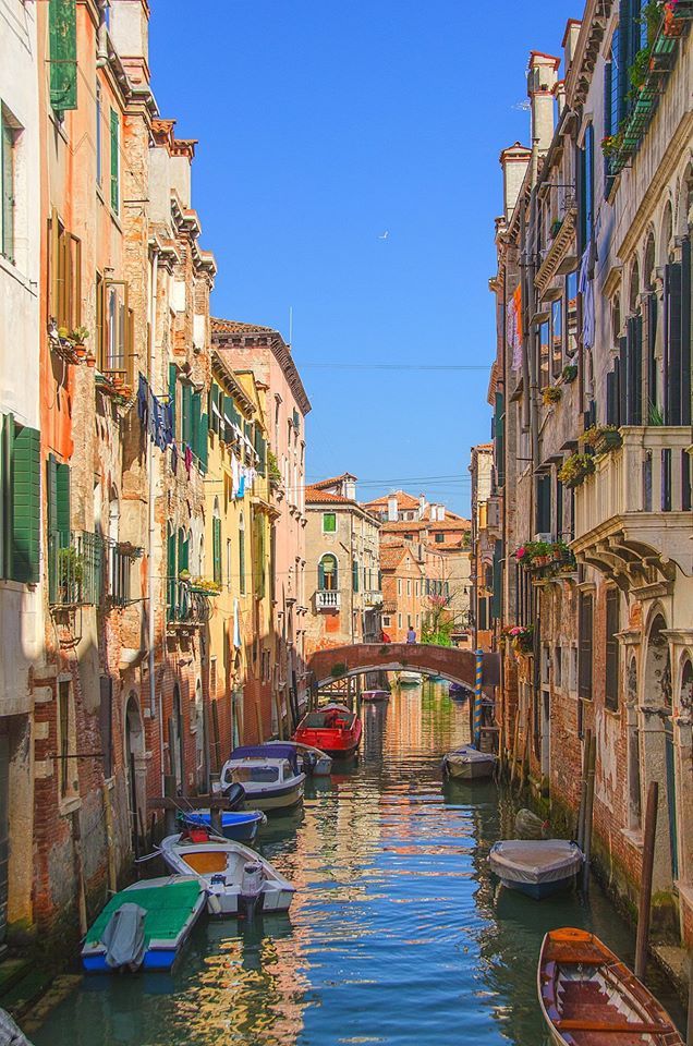 several boats are parked along the side of a narrow canal in venice, italy on a sunny day