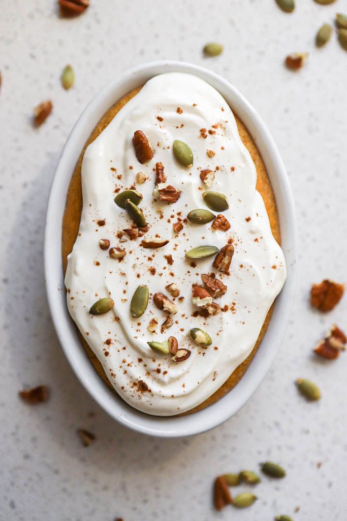 a white bowl filled with cake covered in frosting and nuts on top of a table