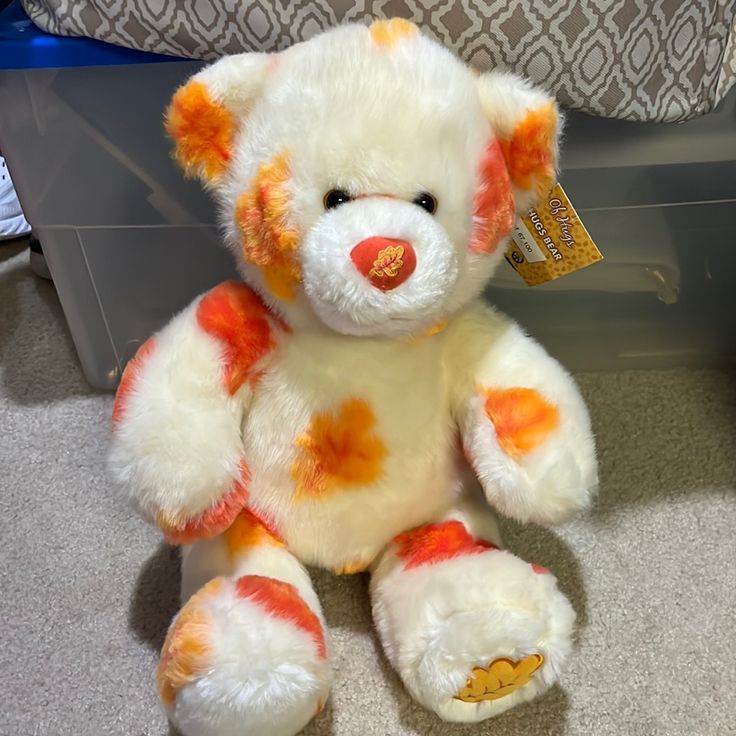 a white and orange teddy bear sitting on the floor