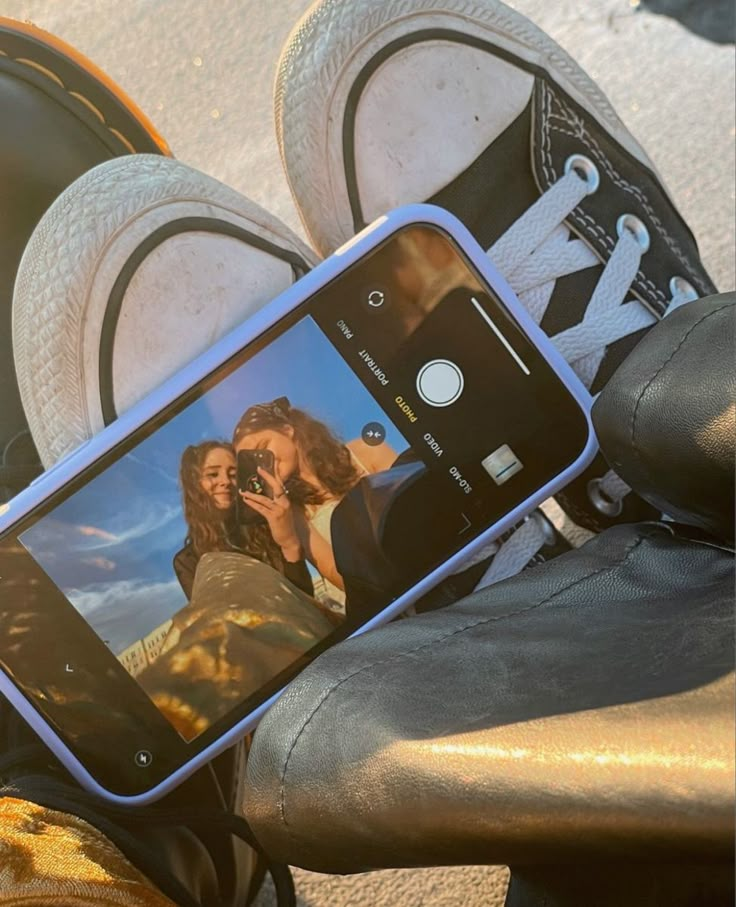 a person taking a photo with their cell phone while sitting on the ground next to some shoes