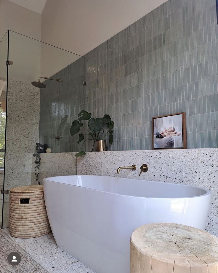 a large white bath tub sitting in a bathroom next to a wooden stool and potted plant