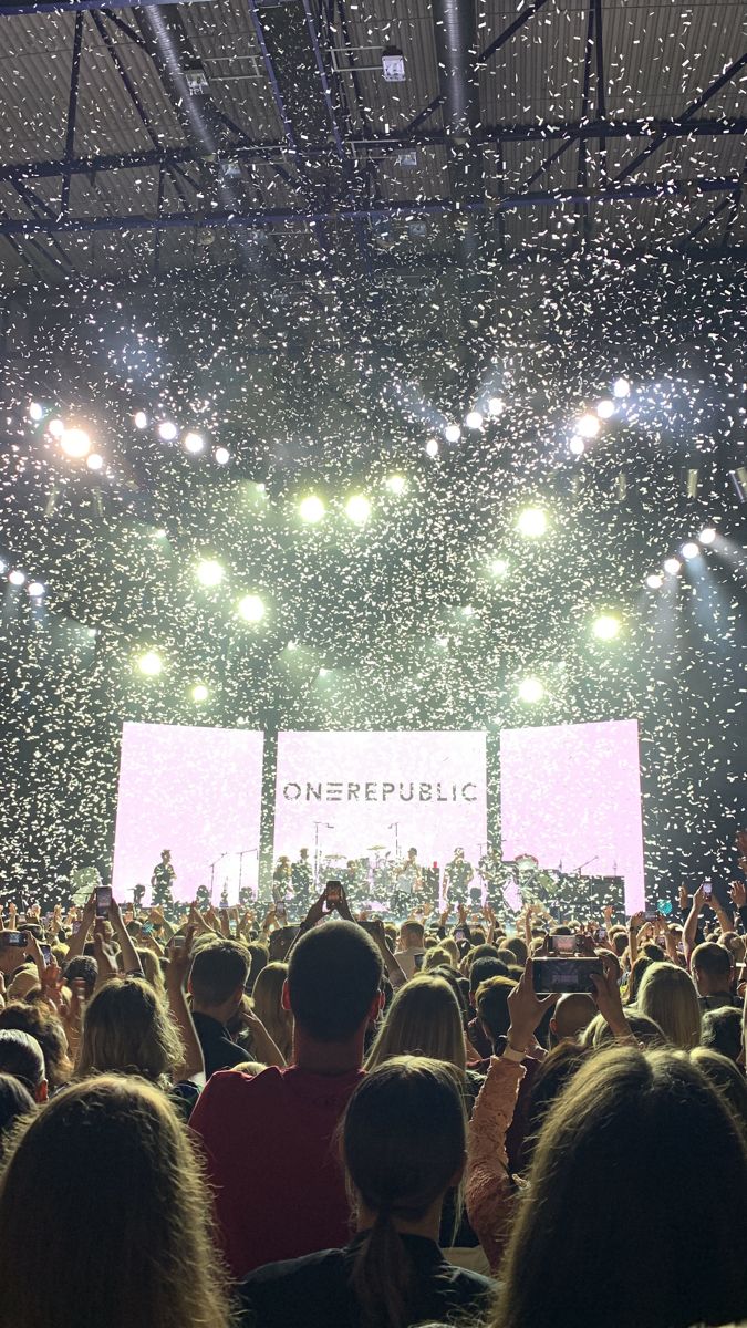 a large crowd at a concert with confetti falling from the ceiling and onlookers