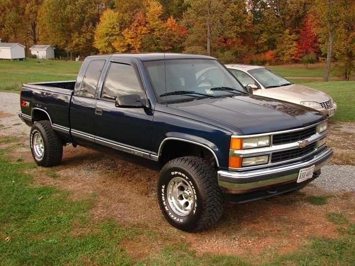 two pickup trucks parked in the grass near trees