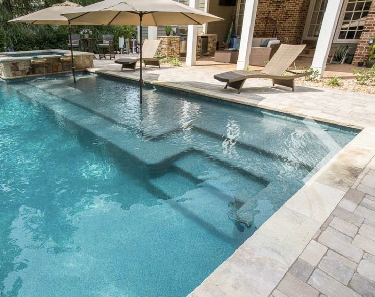 an empty swimming pool with lounge chairs and umbrellas in front of the home's patio