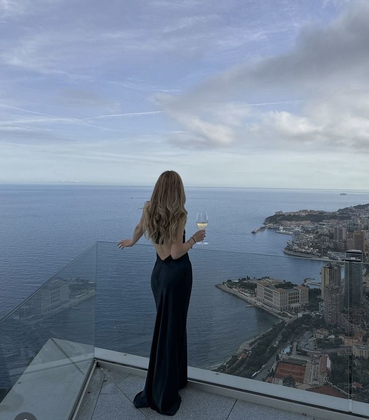 a woman standing on top of a building holding a glass of wine in her hand