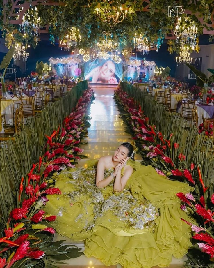 a woman in a yellow dress laying on the ground surrounded by flowers and greenery