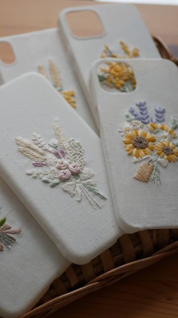 four embroidered phone cases sitting on top of a basket