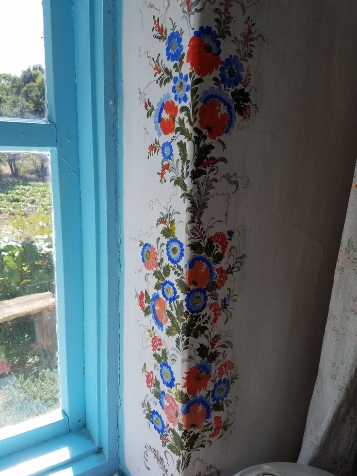 a toilet sitting in front of a window next to a wall with flowers painted on it