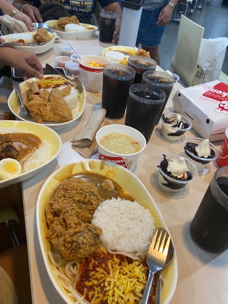 several plates of food on a table with drinks and people in the background eating from bowls