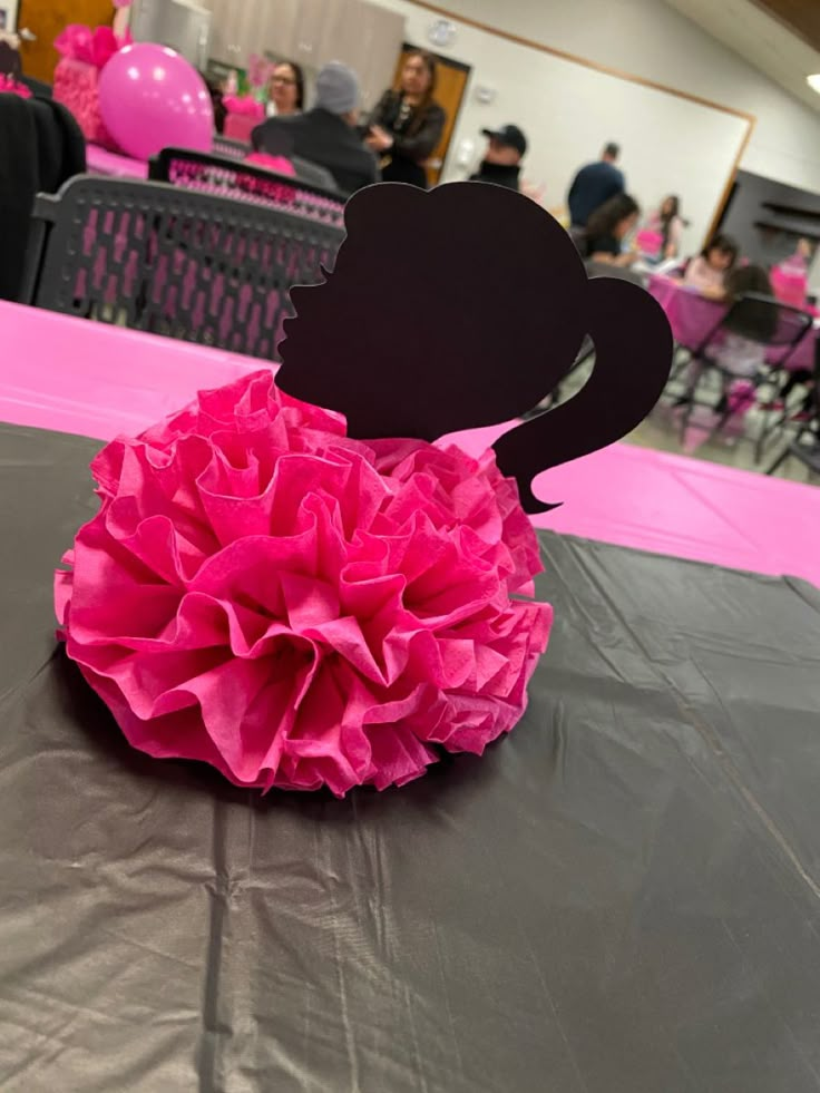 a pink tissue flower sitting on top of a table in a room filled with people