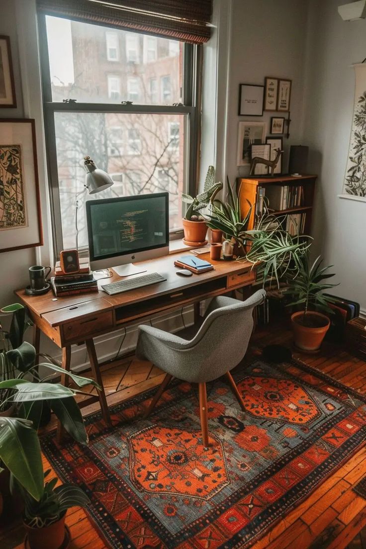 a desk with a computer, chair and potted plants in front of a window