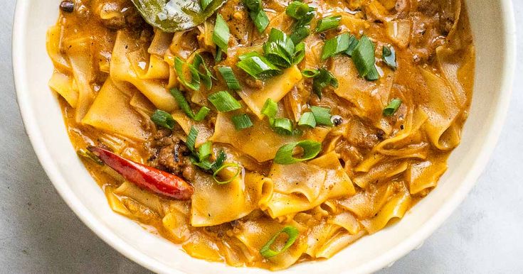 a white bowl filled with pasta and meat covered in sauce, garnished with parsley