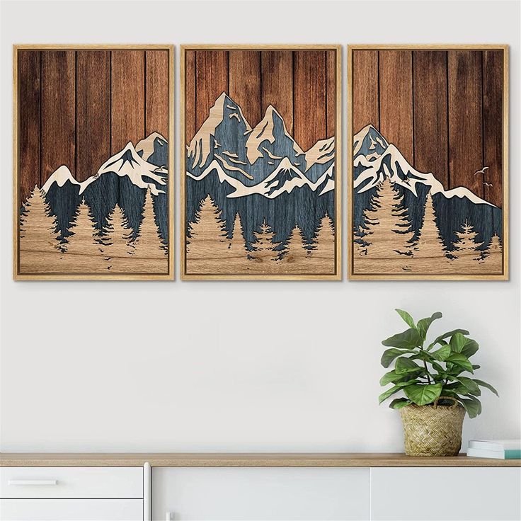 three wooden wall hangings with mountains and pine trees on them in a living room