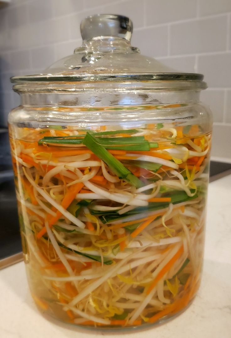 a glass jar filled with assorted veggies on top of a counter