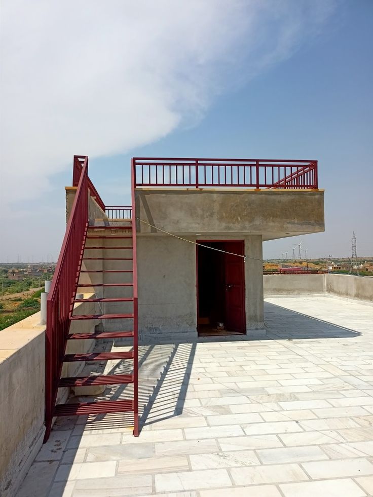 the stairs lead up to an open door at the top of a concrete structure with red railings