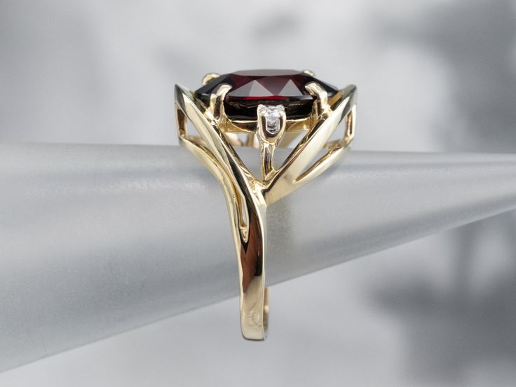 This is a stunning cocktail mounting crafted from shining yellow gold! The ring is really all about the center stone, and the simple styling and accent diamonds create the perfect stage! Deep, crimson red, this garnet is the color of a fine cabernet, poured in a golden glass.Metal: 14K Yellow GoldGem: Garnet 6.50 CaratsGem Measurements: 13.2 x 10.6 mm, OvalAccents: 2 Diamonds totaling .10 Carats, I1 in Clarity, G in ColorRing Size: 6.75Marks: "14KP" Stamped on the inside band Formal Garnet Rings With Gemstone Accents, Elegant Ruby Ring With Polished Finish, Elegant Garnet Ring With Prong Setting, Elegant Garnet Ring With Center Stone, Elegant Ruby Ring With Center Stone For Formal Occasions, Modern Garnet Rings For Formal Occasions, Modern Garnet Rings For Formal Events, Elegant Marquise Gold Ruby Ring, Formal Garnet Gemstone Diamond Ring