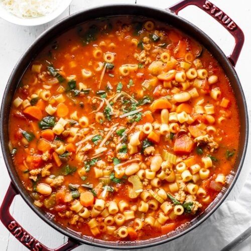 a pot filled with pasta and vegetables on top of a white countertop next to a bowl of soup