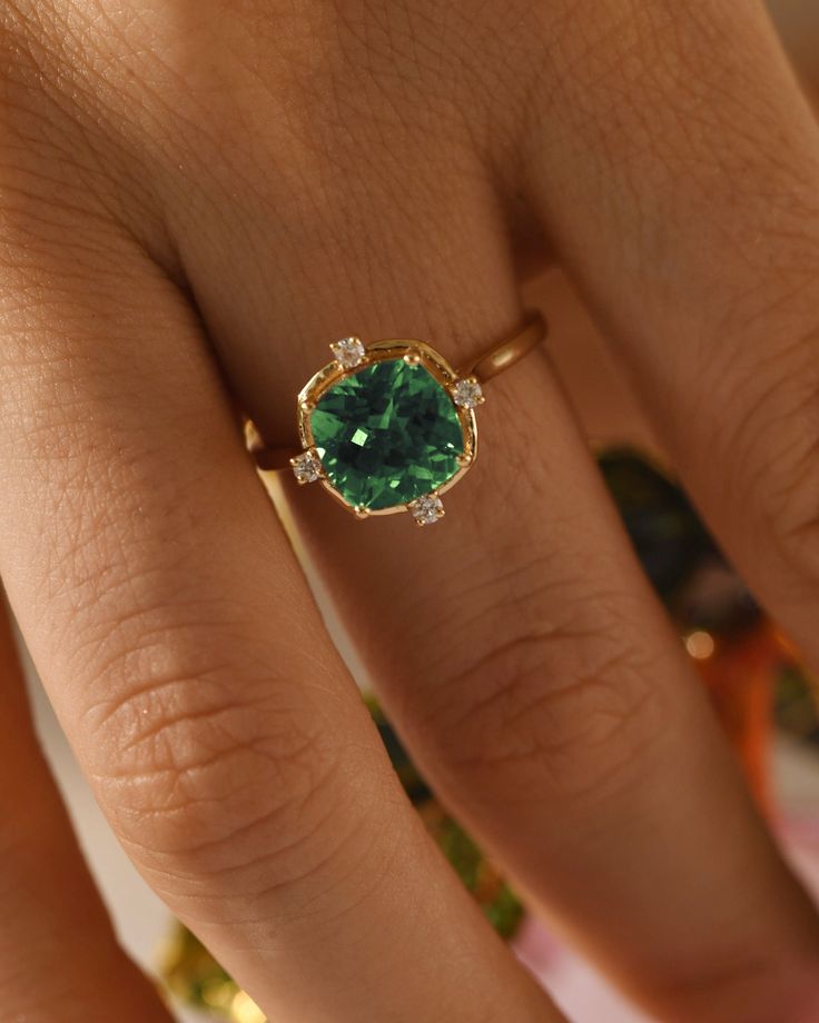 a woman's hand with a green ring on top of her finger and an emerald stone in the middle