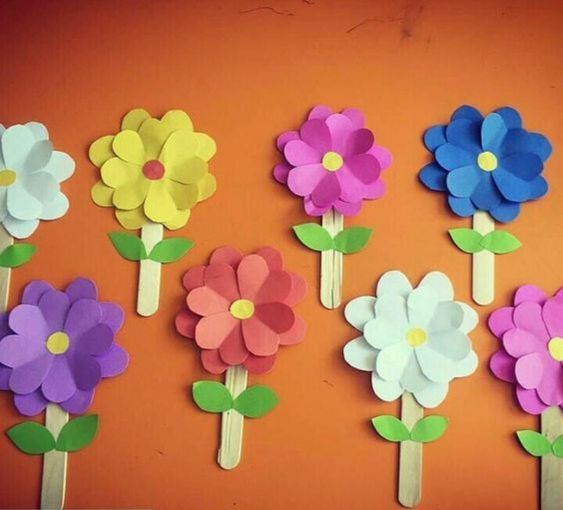 paper flowers are arranged on wooden sticks in front of an orange wall with green leaves