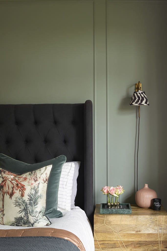 a bedroom with green walls and a black headboard on the bed, next to a night stand