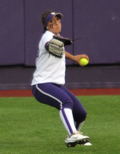 a female baseball player in action on the field with a ball and mitt, ready to throw it