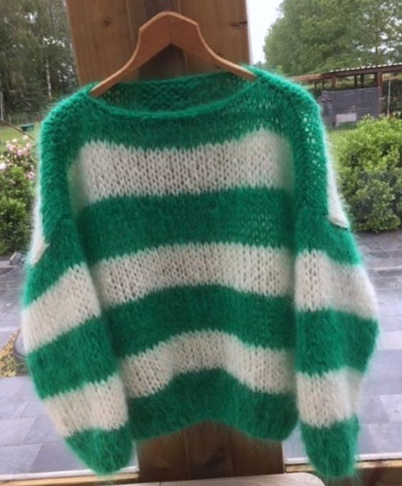 a green and white sweater hanging on a wooden hanger in front of a window