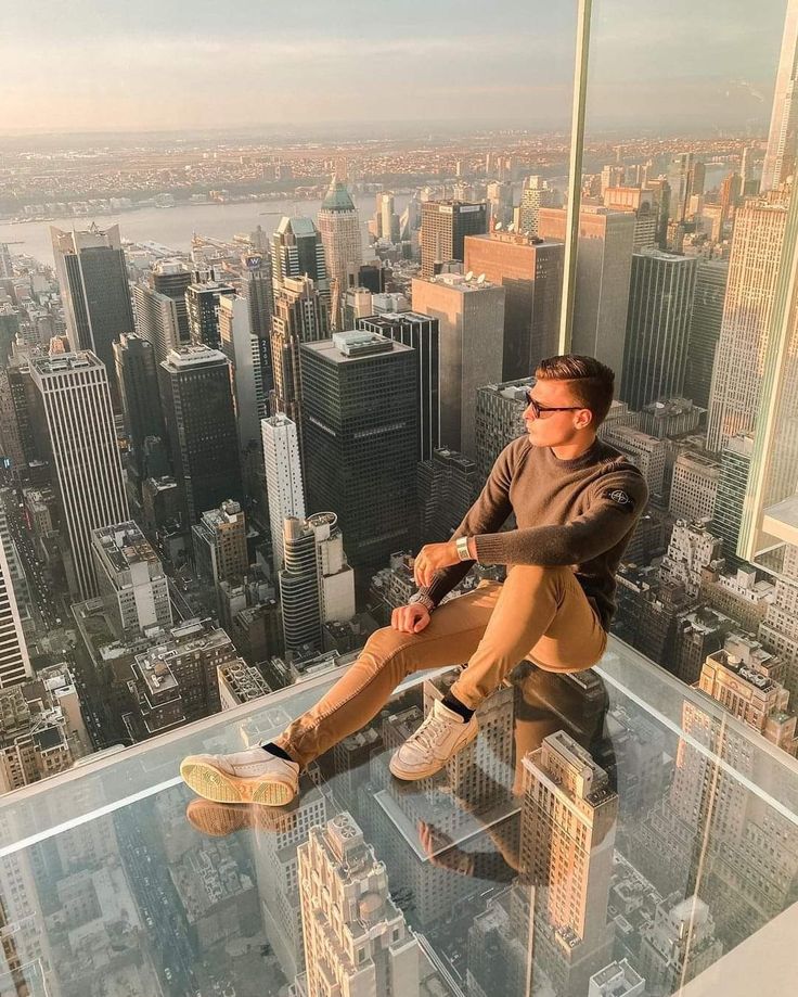 a man sitting on top of a tall building looking down at the city from above