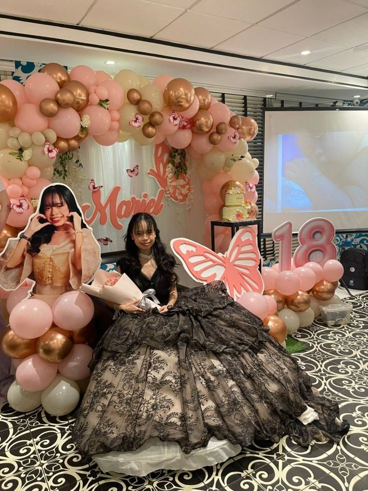 a woman sitting in front of a balloon arch with balloons around her and an image of a butterfly on it