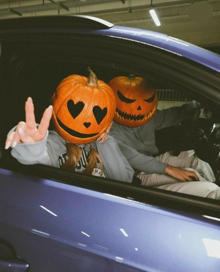 two people in a car with pumpkins on their heads and one holding up the peace sign