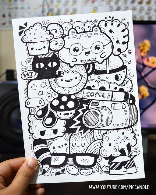 a hand holding up a black and white coloring book with doodles on it in front of a computer screen