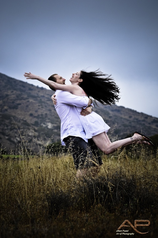 a man and woman are hugging in the middle of a field with mountains in the background