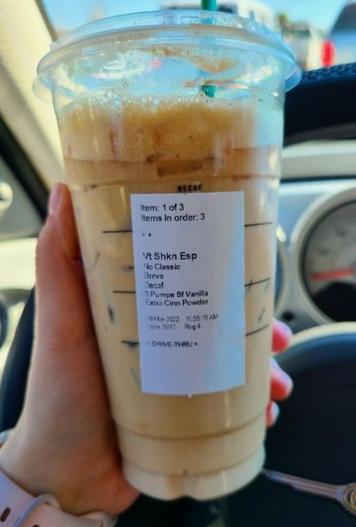 a person holding up a plastic cup filled with liquid on top of a steering wheel