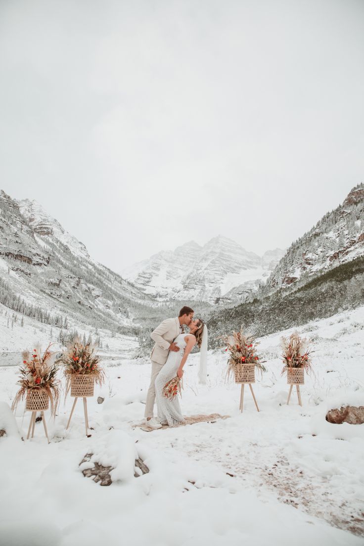 a bride and groom kissing in the snow with mountains in the background at their wedding