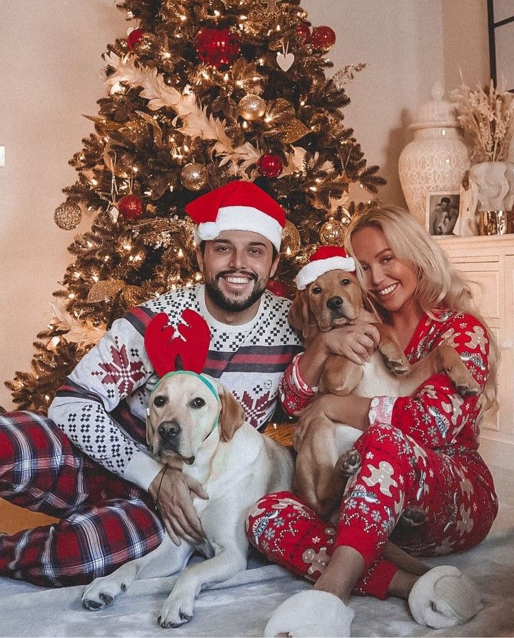 a man and woman sitting next to a christmas tree with two dogs in front of them