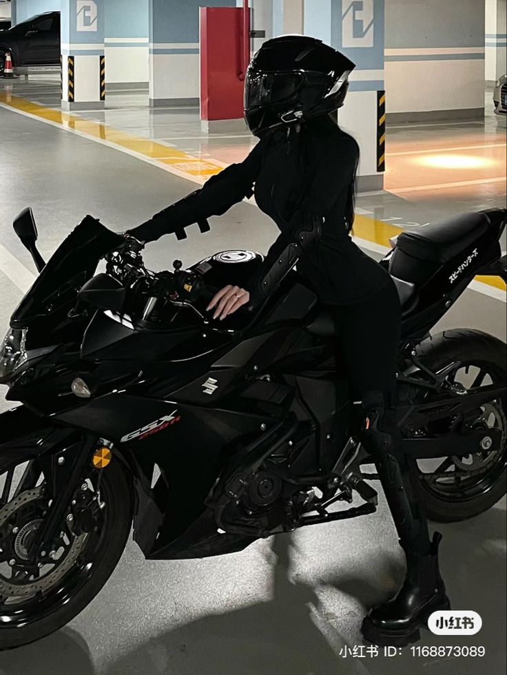 a woman in black riding on the back of a motor bike at an indoor parking lot