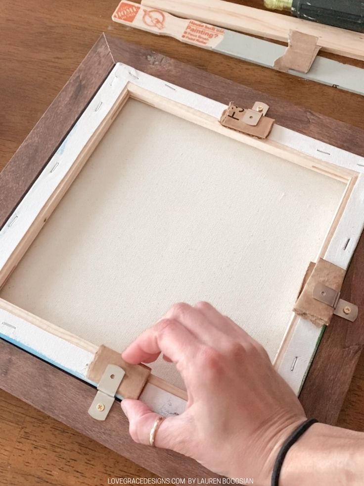 a person is making a frame out of wood and glues it with some scissors