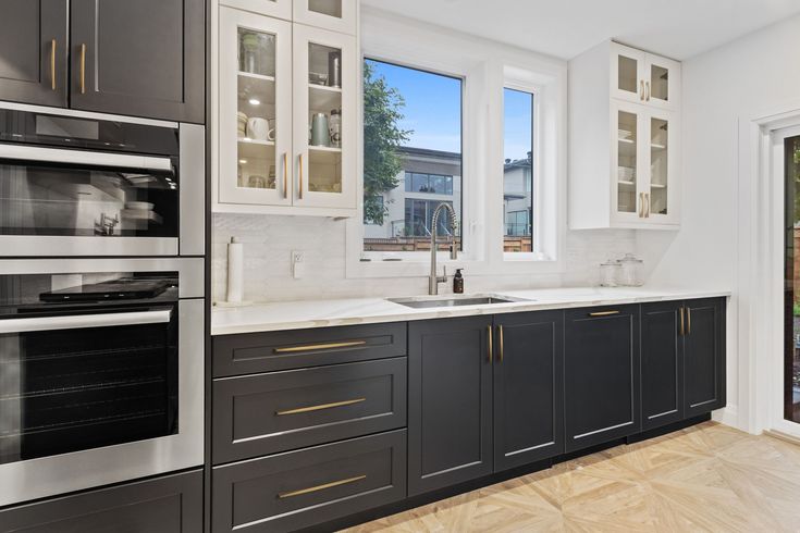 a kitchen with black and white cabinets, stainless steel appliances, and wood flooring